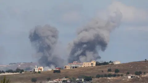Smoke billows in southern above some houses on an incline in Lebanon following an Israeli strike