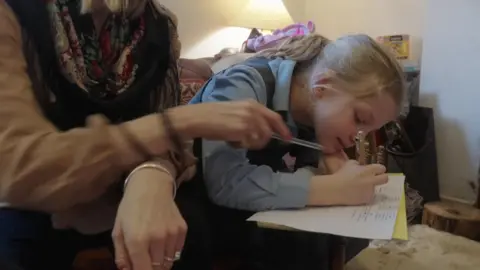 A young girl in uniform writes on a piece of paper