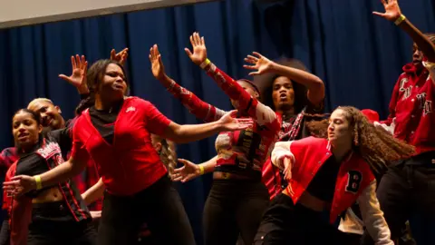 Shanei Stephenson-Harris A group of young people, wearing red tops and black trousers, dancing in the talent show Boroughs United