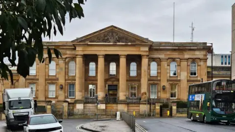 The exterior of a sandstone court building with four pillars outside the main entrance