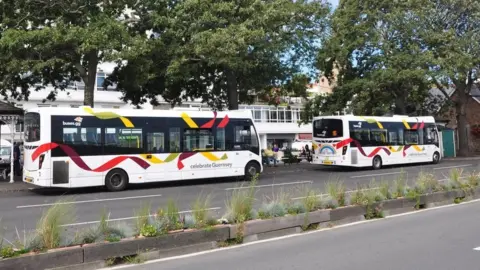 BBC Two white buses with red and yellow livery next to a bus terminus