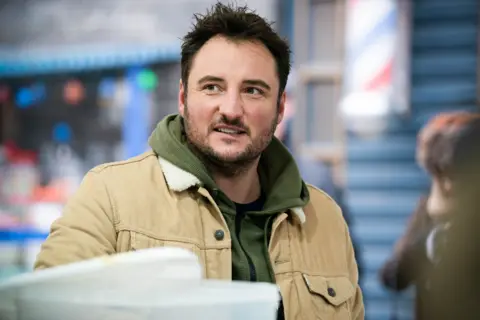 A man in a khaki hoodie and light brown jacket with a fur collar