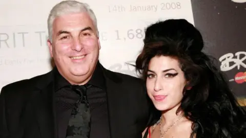 Getty Images A heavy-set grey-haired man standing next to the singer, who has with long dark hair and black winged eyeliner