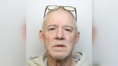 Joseph Pike is looking at the camera and has a piercing in-between is upper eye lid and eye brow. He is wearing glasses on his head.