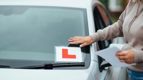 Learner placing an L sign on a car
