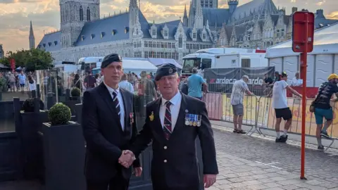 Two men in military uniforms shaking hands. In the background there is a large gothic church.