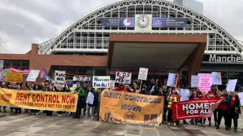 BBC / Kevin Fitzpatrick Protestors hold a range of banners outside Manchester Central, including one which says "Rent controls now".