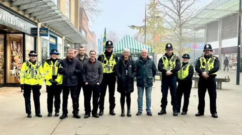 Wiltshire Police The neighbourhood policing team stand in a line in the town centre looking at the camera. Six people are wearing full uniform, whereas five people are in plain clothes.