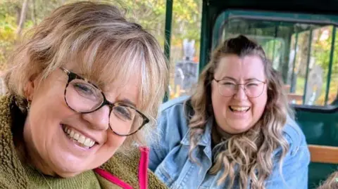 Angie Emery Two women with glasses smiling, one with light blonde short hair and one with long brown hair. 