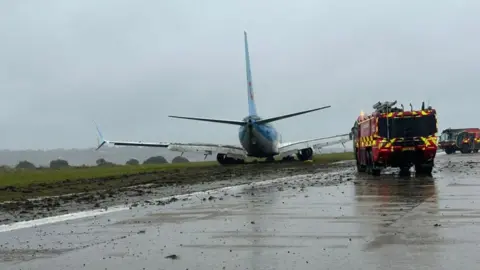 A TUI jet on the grass verge at Leeds Bradford Airport with two fire engines next to it 