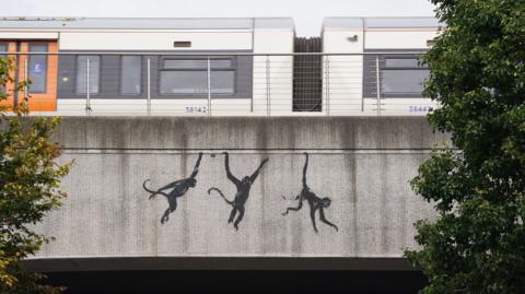 Three painted monkeys swinging from a bridge