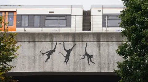 PA Media Three painted monkeys swinging from a bridge