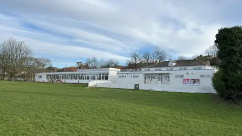 Somerset Council The picture shows the outside of Tor Sports and Leisure facility. The building is white in colour and there is grass in the foreground. 