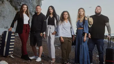 Channel 4 The participants of Go Back To Where You Came From on Dover beach. L-R is Chloe, Dave, Bushra, Jess, Mathilda and Nathan. They all have suitcases as if prepared to go on holiday and stand on the shingle in front of the white cliffs. 