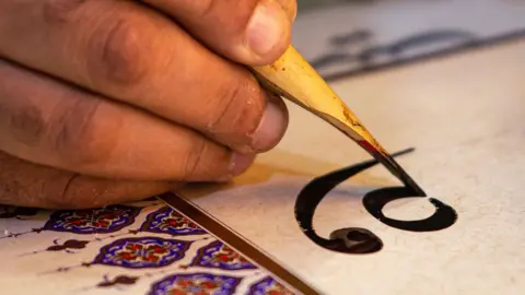 A man uses a stylus to produce a sample of Arabic calligraphy.