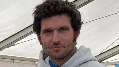 A close-up image of Guy Martin who is wearing a grey hoodie and standing in a marquee.