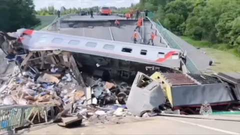 A derailed passenger carriage is seen surrounded by debris on the collapsed bridge