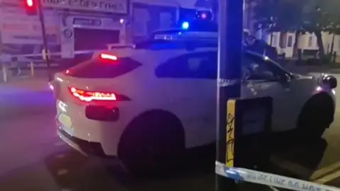 Car driving into police cordon with shops in the background