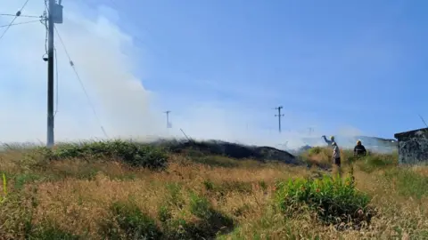 Finbar Gallagher A number of firefighters pictured tackling a gorse fire in a large grassy field. 