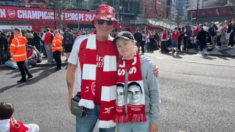 Fans Bill Tasselli and Daisy Goodhand stand outside the stadium wearing Arsenal scarves and looking at the camera