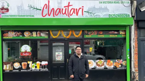 A man wearing glasses and stood in front of a restaurant.