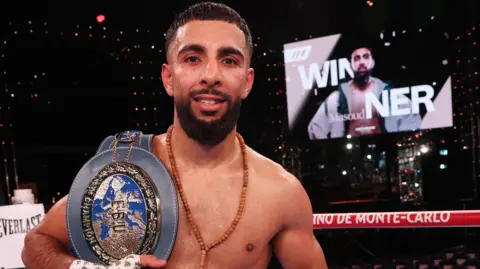 A boxer with a title belt. The grey belt has a blue badge on it.