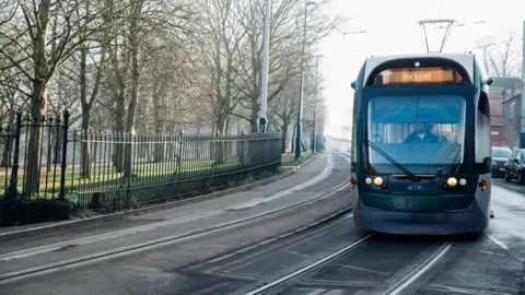 Tram running along street tracks past an area of parkland