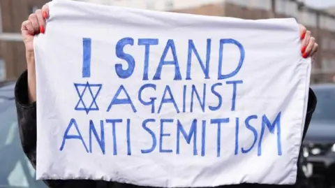PA Media A member of the public holds up a sign with the words 'I stand against antisemitism'
