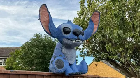 Matt Jerome Uma efígie do personagem da Disney Stitch sentado na cerca do jardim.