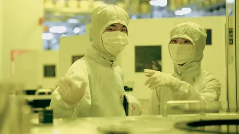 Employees of SK Hynix in discussion while dressed in white protective gear in a clean room 