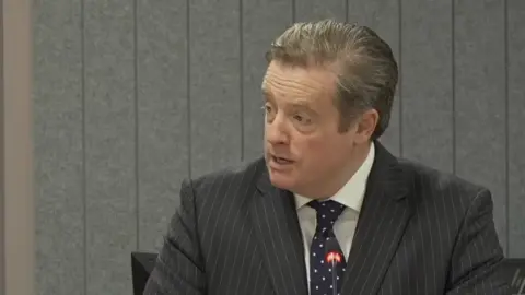 Eljamel Inquiry Jamie Dawson KC, wearing a grey pinstriped suit and a blue polka dot tie with a white shirt.