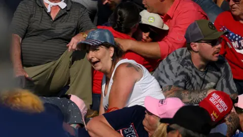 Getty Images Crowd members stare in disbelief as Trump is hurried away