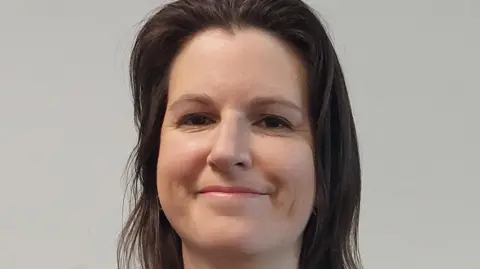 Shropshire Council Woman with dark hair grinning for an official portrait photograph in front of a grey background.