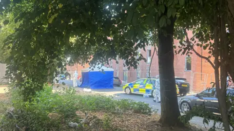 A blue police tent with man walking in white forensic uniforms
