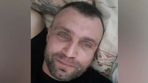 Police Scotland Jacek Dembinski, man with stubble, smiling at the camera, with his arm resting behind the head.