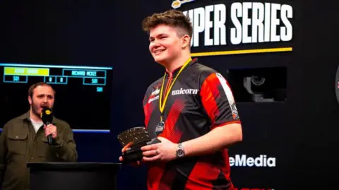 Supplied A young man on stage with a trophy and a medal around his neck.