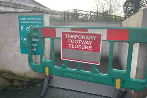 Steve Beech/BBC A green barrier at the start of the bridge which reads on a red sign: TEMPORARY FOOTWAY CLOSURE