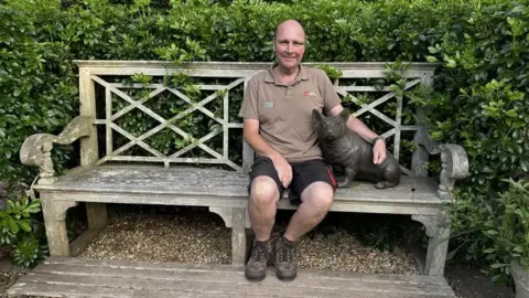 Jo Burn/BBC Philip Oostenbrink, head gardener, on the bench in the gardens of Walmer Castle next to a corgi where the late Queen Mother would sit