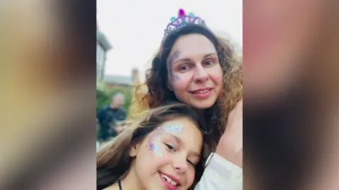 Family handout A woman is taking a selfie with a little girl. They both have long brown hair and are smiling and have purple and silver glitter down the side of their faces. The woman is wearing a purple tiara and the background is blurred.