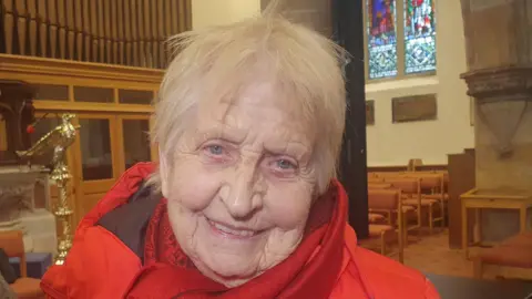Daphne smiling at the camera. She is wearing a red coat and red scarf.