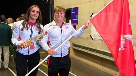 ERICA BELLHOUSE Laura and Alfie standing side by side holding the baton and the Manx flag.