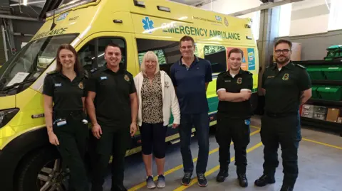 South Central Ambulance Service (L-R), Caitlyn, Sam, Wendy, Dave, Kieran and Craig. Caitlyn, Sam, Kieran and Craig wearing paramedic uniform whilst Wendy is wearing black cropped trousers, a leopard print top and white zip jacket and her husband Dave standing to her right is wearing blue jeans and a blue polo shirt.
