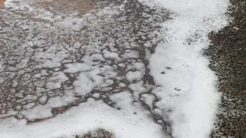 A liquid spill on the road with thin foam on the top