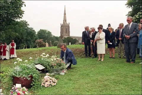 Getty Images A crowd of mourners look on as flowers are laid at a garden of remembrance for Celine Figard. The Spire of St Andrew's church can be seen in the background also choristers from the church stand on the grass  