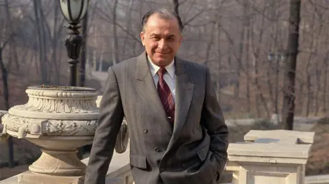 Peter Turnley/Corbis/VCG via Getty Images Iliescu poses and looks straight down the camera with a slight smile. He is leaning on a stone balcony and wearing a grey suit.