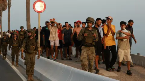 Members of the military escort migrants in Ceuta, Spain, following recent mass crossings of migrants on foot and by sea from Morocco into Spanish territory.