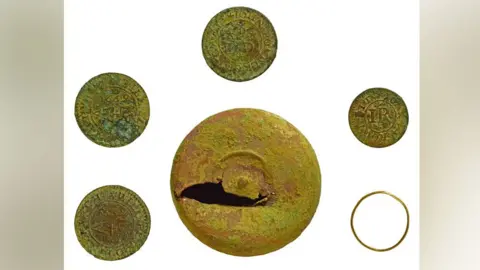 British Museum's Portable Antiquities Scheme A copper alloy token box with four copper alloy trading tokens and a gold ring. The trading box, which has a gouge out of it, is in the middle and the tokens and ring are placed around the box, evenly spaced.
