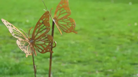 A close-up of a delicate, gold-coloured butterfly ornament against a grassy backdrop.