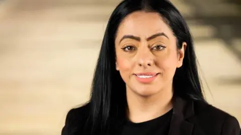 Arooj Shah, who has black hair, poses smiling for a photograph wearing all black. 