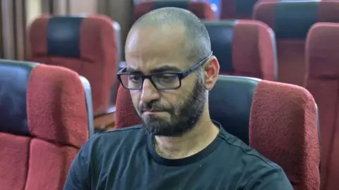 Getty Images Tigran Gambaryan, wearing a black T-shirt and looking down, sitting on a red seat in court in Abuja, Nigeria - April 2024